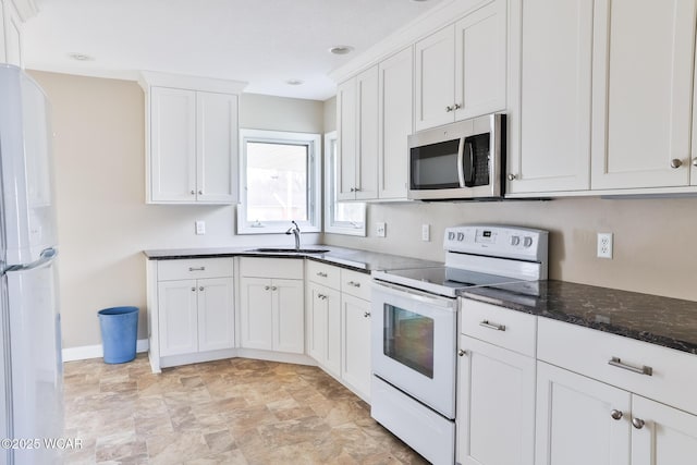 kitchen with white cabinets, a sink, dark stone counters, white appliances, and baseboards