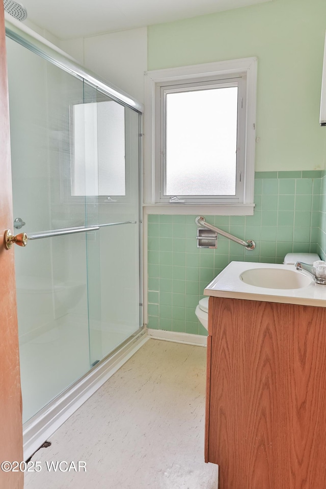 bathroom featuring tile walls, toilet, wainscoting, a shower stall, and vanity