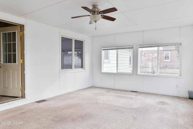 carpeted spare room featuring baseboards, ceiling fan, visible vents, and a wealth of natural light