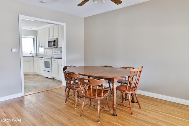 dining room with light wood-type flooring, a ceiling fan, and baseboards