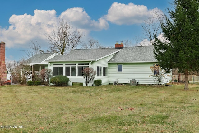 back of property with central air condition unit, a sunroom, a yard, roof with shingles, and a chimney