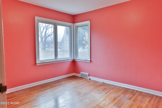 empty room featuring wood finished floors, visible vents, and baseboards