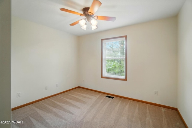 carpeted spare room with visible vents, baseboards, and ceiling fan