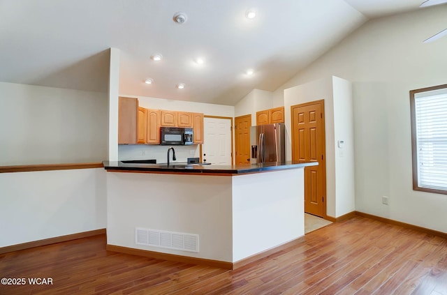 kitchen featuring dark countertops, black microwave, light wood finished floors, stainless steel refrigerator with ice dispenser, and visible vents