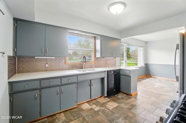 kitchen with tasteful backsplash, a sink, light countertops, black dishwasher, and stainless steel fridge