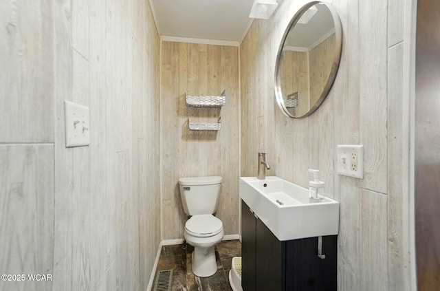bathroom with toilet, vanity, visible vents, wooden walls, and crown molding
