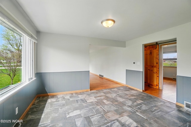 unfurnished room with visible vents, a healthy amount of sunlight, a barn door, and stone finish flooring
