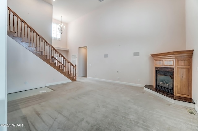 unfurnished living room with light colored carpet, visible vents, stairway, a high ceiling, and a high end fireplace