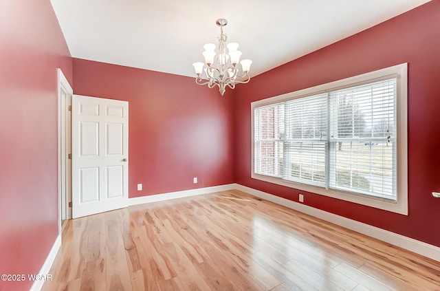 unfurnished room with a notable chandelier, light wood-type flooring, and baseboards