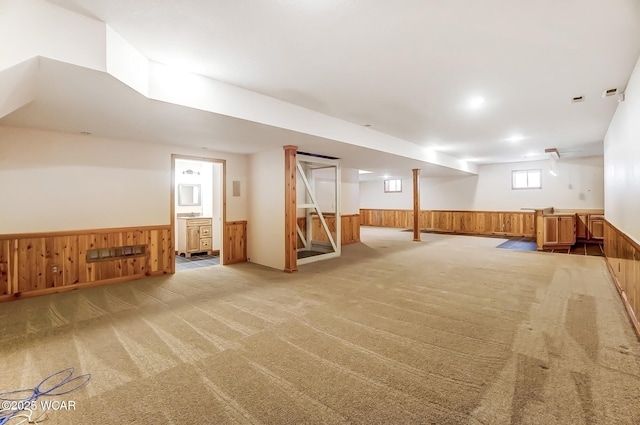 below grade area featuring light carpet, a wainscoted wall, and wooden walls