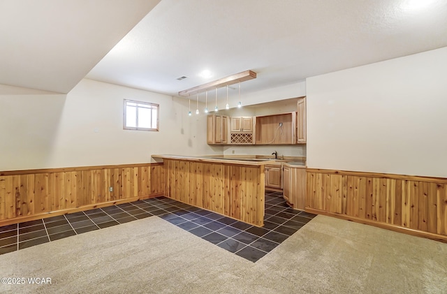 kitchen with wooden walls, a wainscoted wall, dark tile patterned floors, and light brown cabinetry