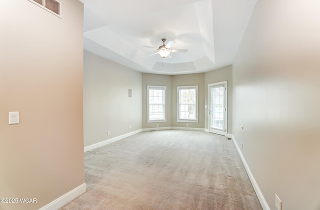 spare room with light colored carpet, visible vents, a ceiling fan, baseboards, and a tray ceiling