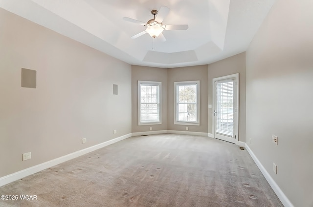 spare room featuring a raised ceiling, light colored carpet, ceiling fan, and baseboards