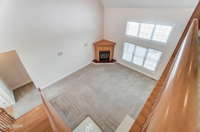 unfurnished living room featuring a fireplace with raised hearth, light colored carpet, a towering ceiling, and baseboards