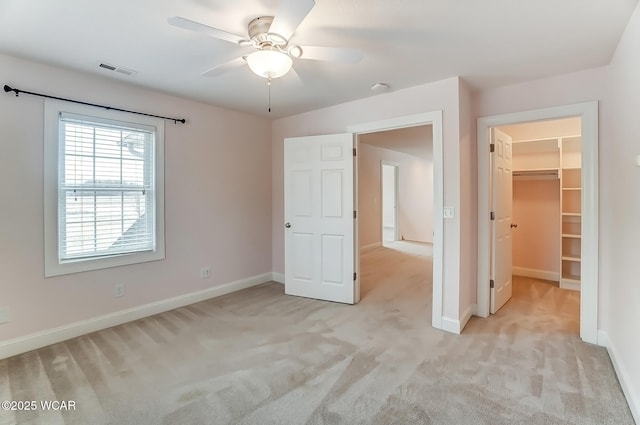 unfurnished bedroom featuring a closet, visible vents, light colored carpet, a spacious closet, and baseboards