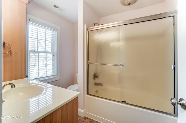 bathroom featuring visible vents, toilet, vanity, and combined bath / shower with glass door