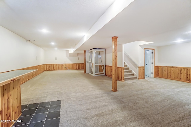 finished below grade area featuring carpet floors, wooden walls, stairway, and wainscoting