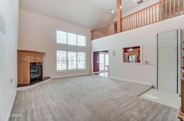 unfurnished living room featuring light carpet, a high ceiling, a high end fireplace, and baseboards