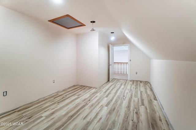 additional living space featuring attic access, light wood-type flooring, and vaulted ceiling