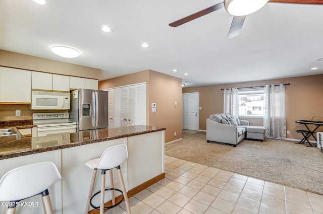 kitchen featuring white appliances, light carpet, dark stone countertops, white cabinets, and a kitchen bar