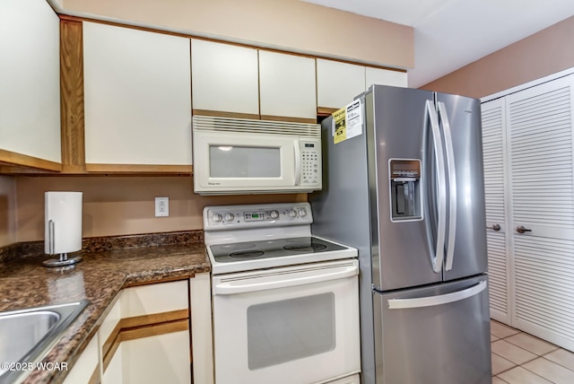 kitchen featuring sink, white appliances, dark stone countertops, white cabinets, and light tile patterned flooring