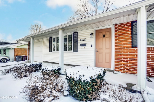 snow covered property entrance featuring a garage