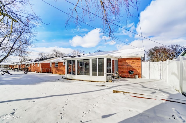 snow covered rear of property with a sunroom