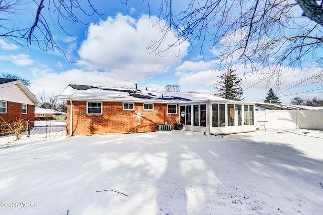 snow covered back of property with central AC unit and a sunroom