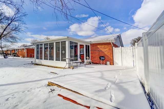 snow covered back of property featuring a sunroom