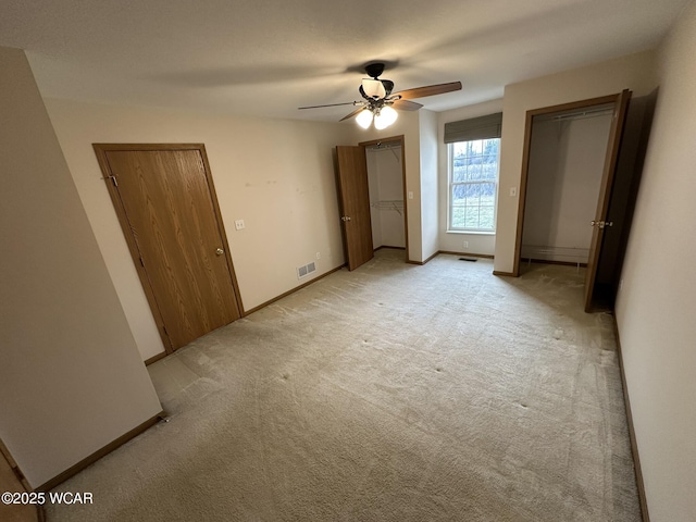 unfurnished bedroom with light carpet, two closets, and ceiling fan