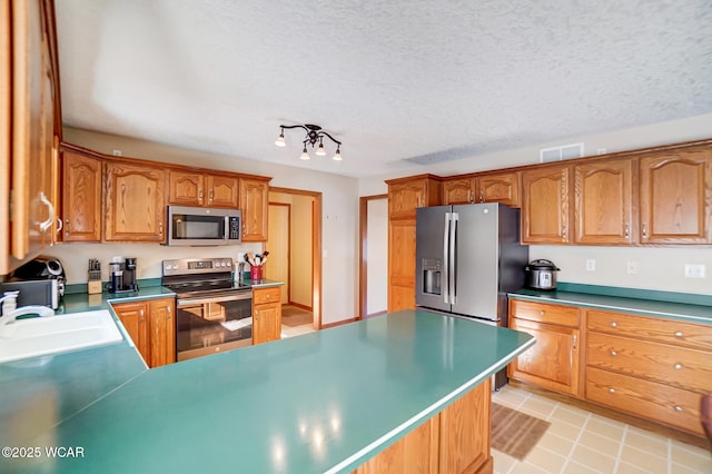 kitchen with appliances with stainless steel finishes, sink, light tile patterned floors, and a textured ceiling