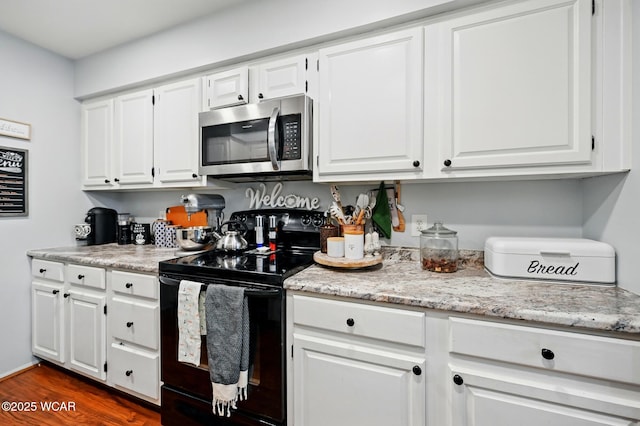 kitchen with stainless steel microwave, black electric range oven, dark wood finished floors, white cabinetry, and light stone countertops