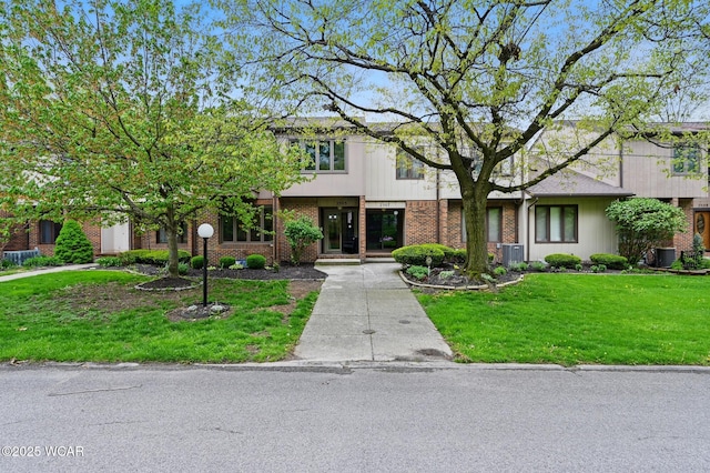 view of front of house with central air condition unit, brick siding, and a front yard