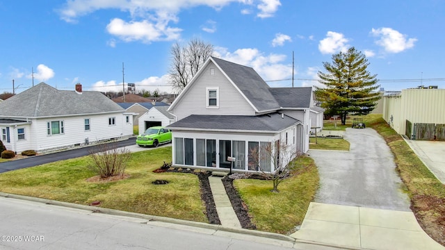 view of front of home with aphalt driveway, a shingled roof, a front yard, and a sunroom