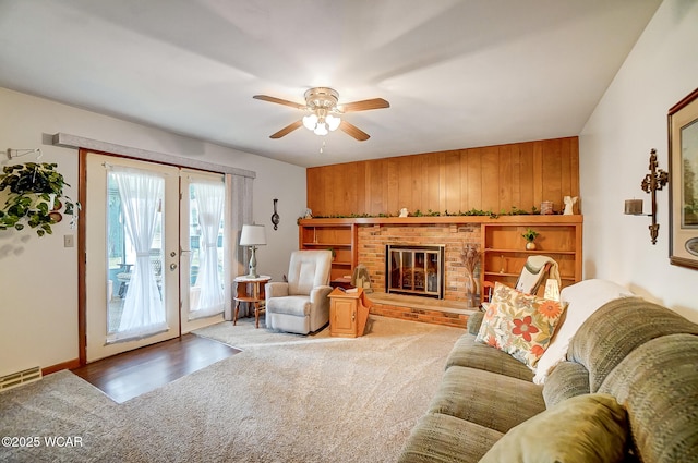 living room featuring a fireplace, wood walls, carpet floors, ceiling fan, and french doors