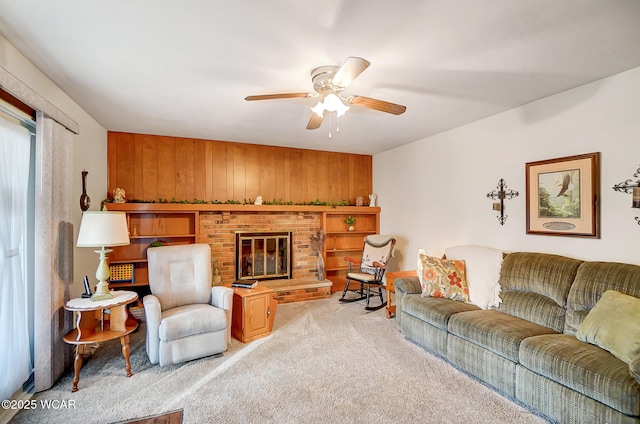 carpeted living room featuring a brick fireplace, wooden walls, and ceiling fan