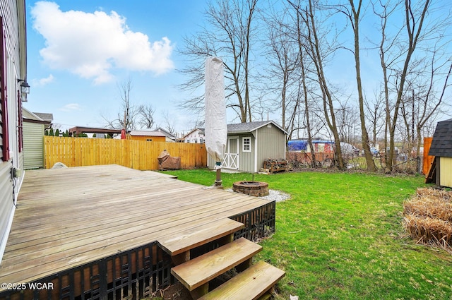 view of yard featuring a storage unit, a wooden deck, a fenced backyard, an outbuilding, and a fire pit