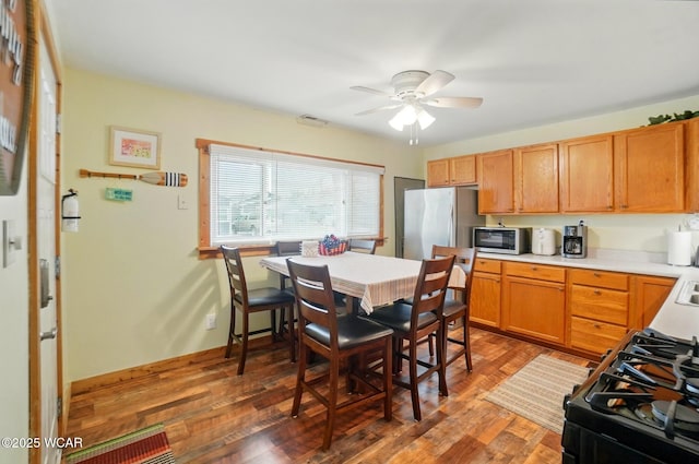 kitchen with wood finished floors, baseboards, light countertops, a ceiling fan, and stainless steel appliances