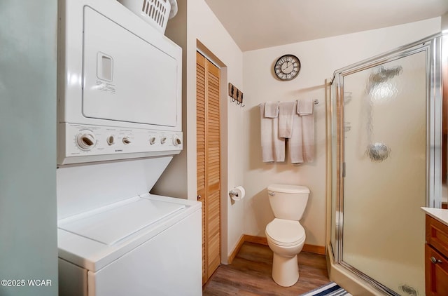 full bath featuring a shower stall, wood finished floors, baseboards, toilet, and stacked washer and clothes dryer