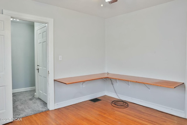 empty room with hardwood / wood-style floors, built in desk, and ceiling fan