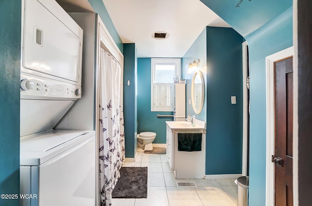 bathroom featuring tile patterned flooring, vanity, toilet, and stacked washer / dryer