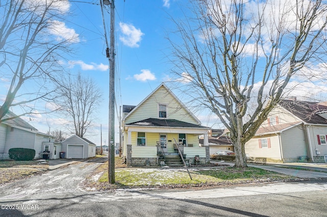 bungalow-style home with a garage, a porch, and an outbuilding