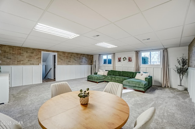 carpeted dining space featuring visible vents, brick wall, a paneled ceiling, and a wainscoted wall