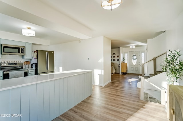 kitchen featuring light countertops, backsplash, light wood-style floors, and appliances with stainless steel finishes