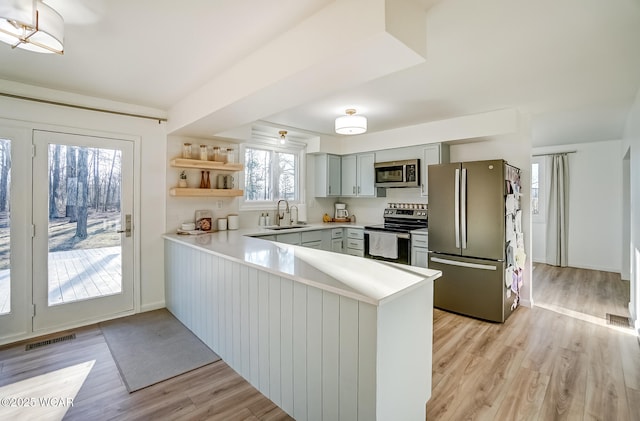 kitchen with a peninsula, a sink, light countertops, appliances with stainless steel finishes, and light wood-type flooring