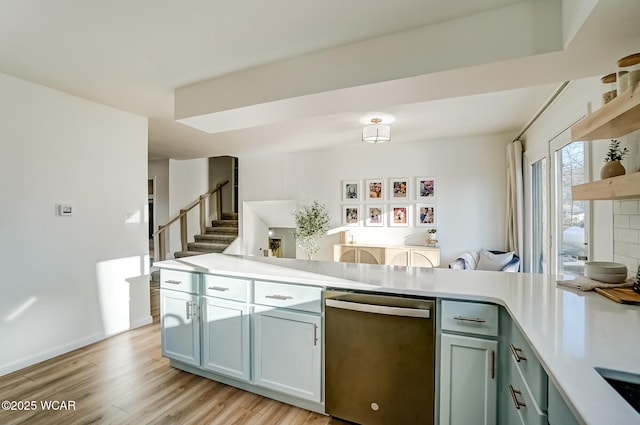 kitchen with light wood finished floors, open shelves, a peninsula, light countertops, and stainless steel dishwasher