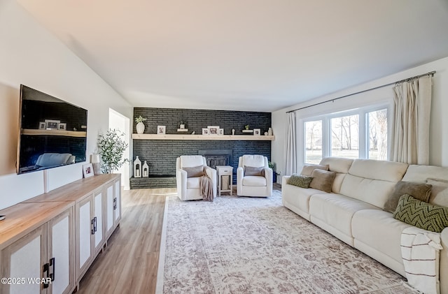 living room with a brick fireplace, light wood-type flooring, and brick wall