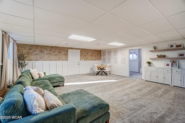 living area with a wainscoted wall, a paneled ceiling, carpet, and brick wall