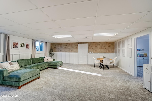 carpeted living room featuring a drop ceiling and a wainscoted wall