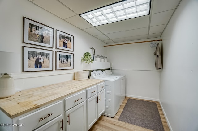 clothes washing area with baseboards, cabinet space, light wood-style floors, and washer and clothes dryer